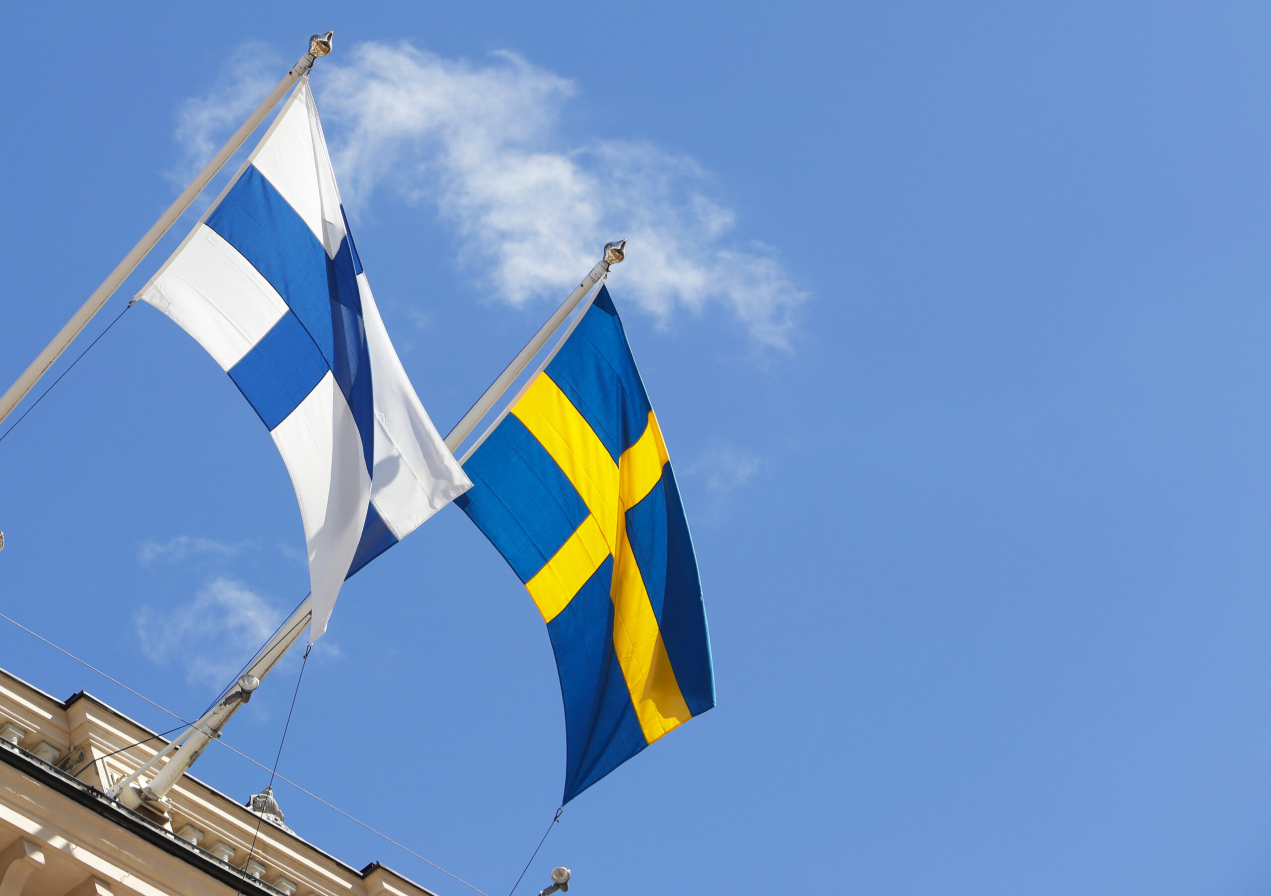 Finska respektive svenska flaggan vajar på flaggstänger på en byggnad
