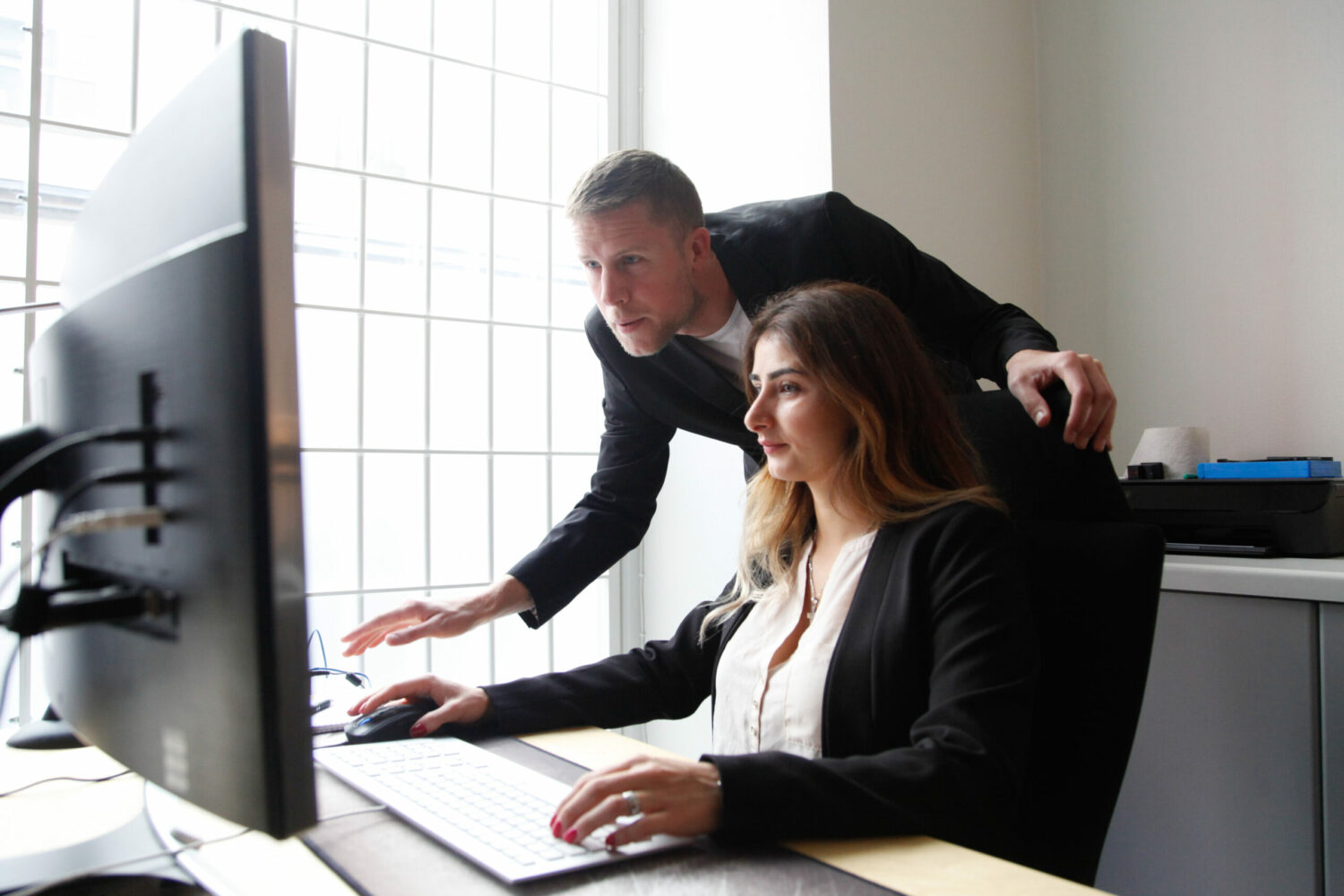 En kvinna sitter vid en dator, en man visar henne något på skärmen