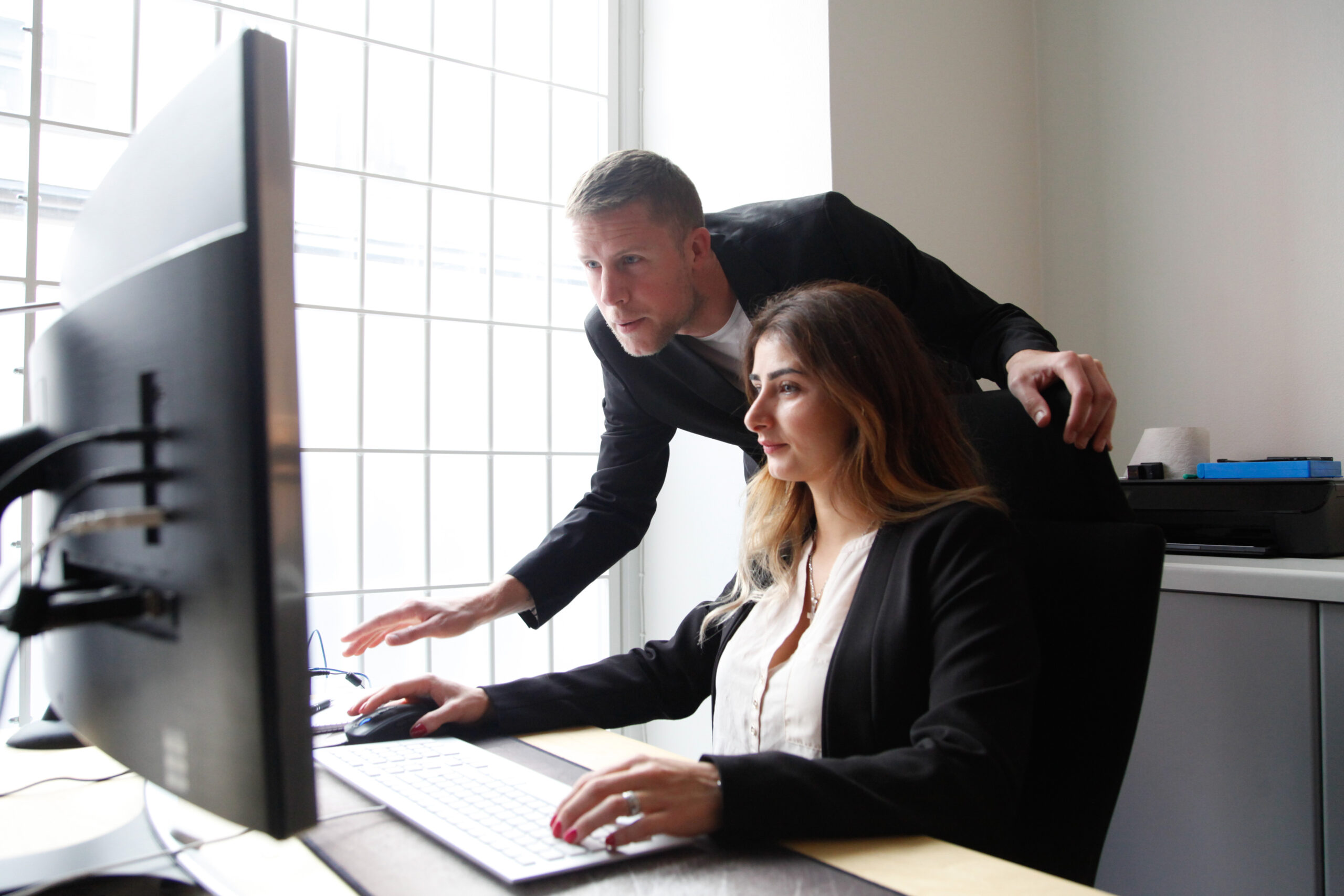 En kvinna sitter vid en dator, en man visar henne något på skärmen